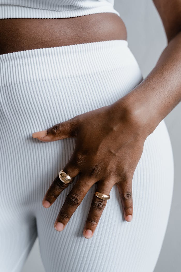 Close-up of a woman's hand with gold rings on white ribbed leggings, showcasing fashion elegance.